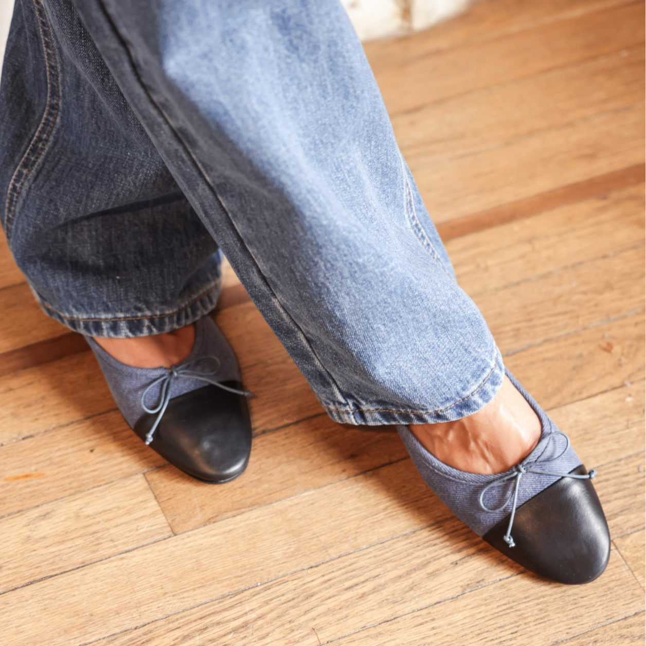 Denim and black leather flats on someone wearing jeans standing on a wooden floor.