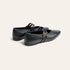 A pair of black leather Mary Jane flats with double straps and small gold-tone buckle details, shown from a three-quarters angle on a light cream background.