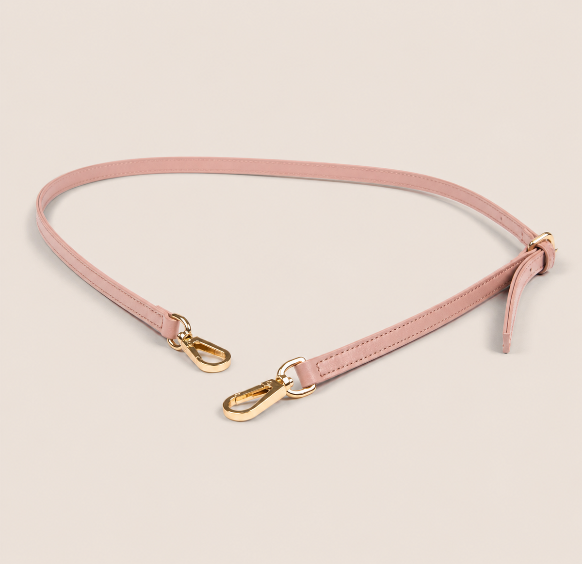 Pink shoulder strap with gold hardware on a beige background