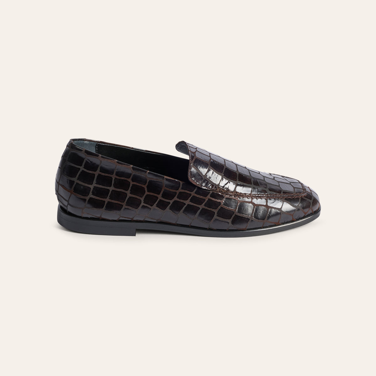 A single dark brown crocodile-embossed leather loafer shown in a side profile on a light beige background.