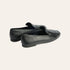 A pair of black leather penny loafers with a tassel detail, shown from a three-quarters rear angle on a light gray studio background.