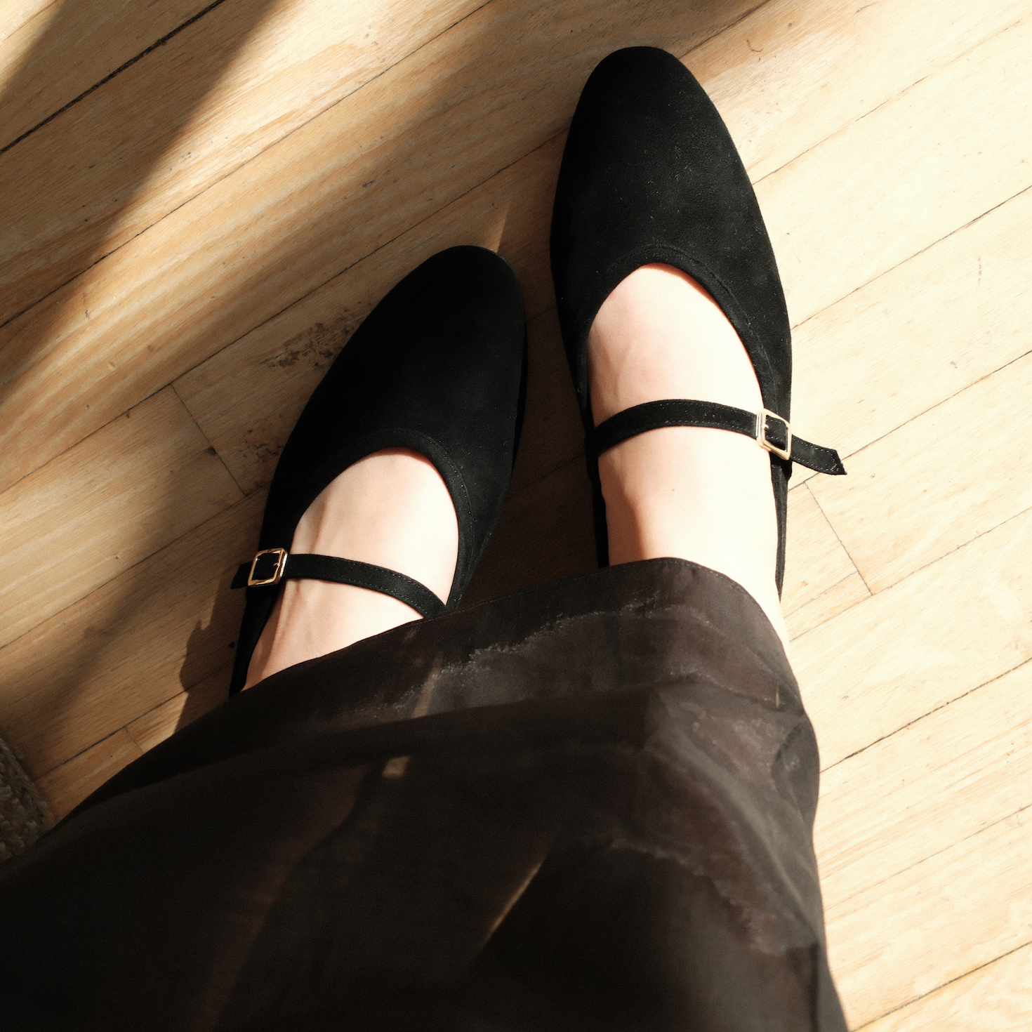 Black shoes with thin straps worn on a wooden floor