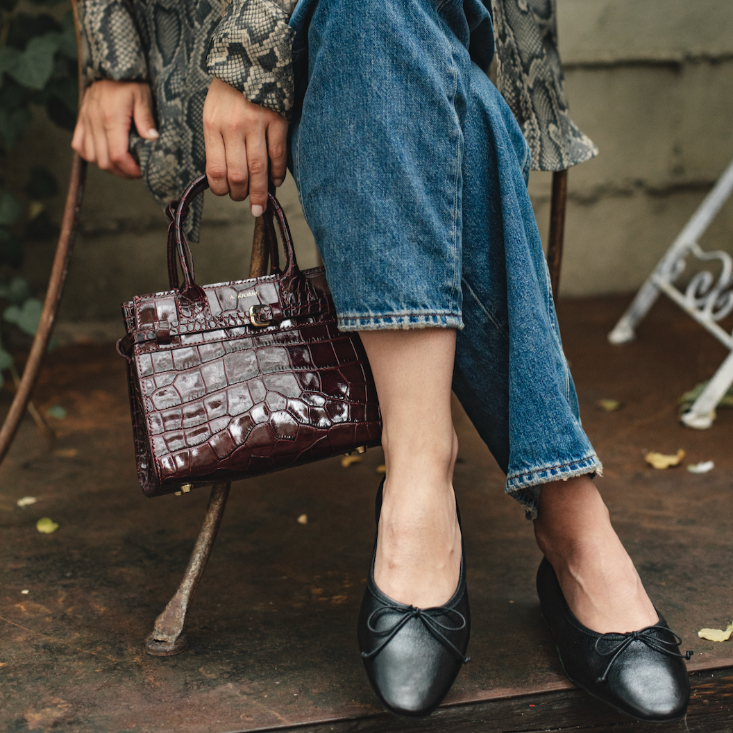 Person wearing a patterned coat, blue jeans, and black shoes, holding a brown handbag.