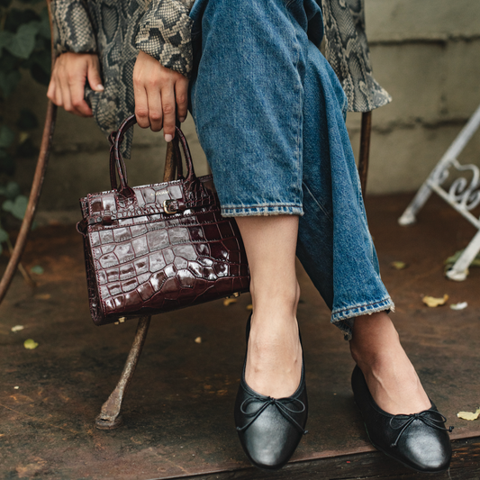Person wearing a patterned coat, blue jeans, and black shoes, holding a brown handbag.