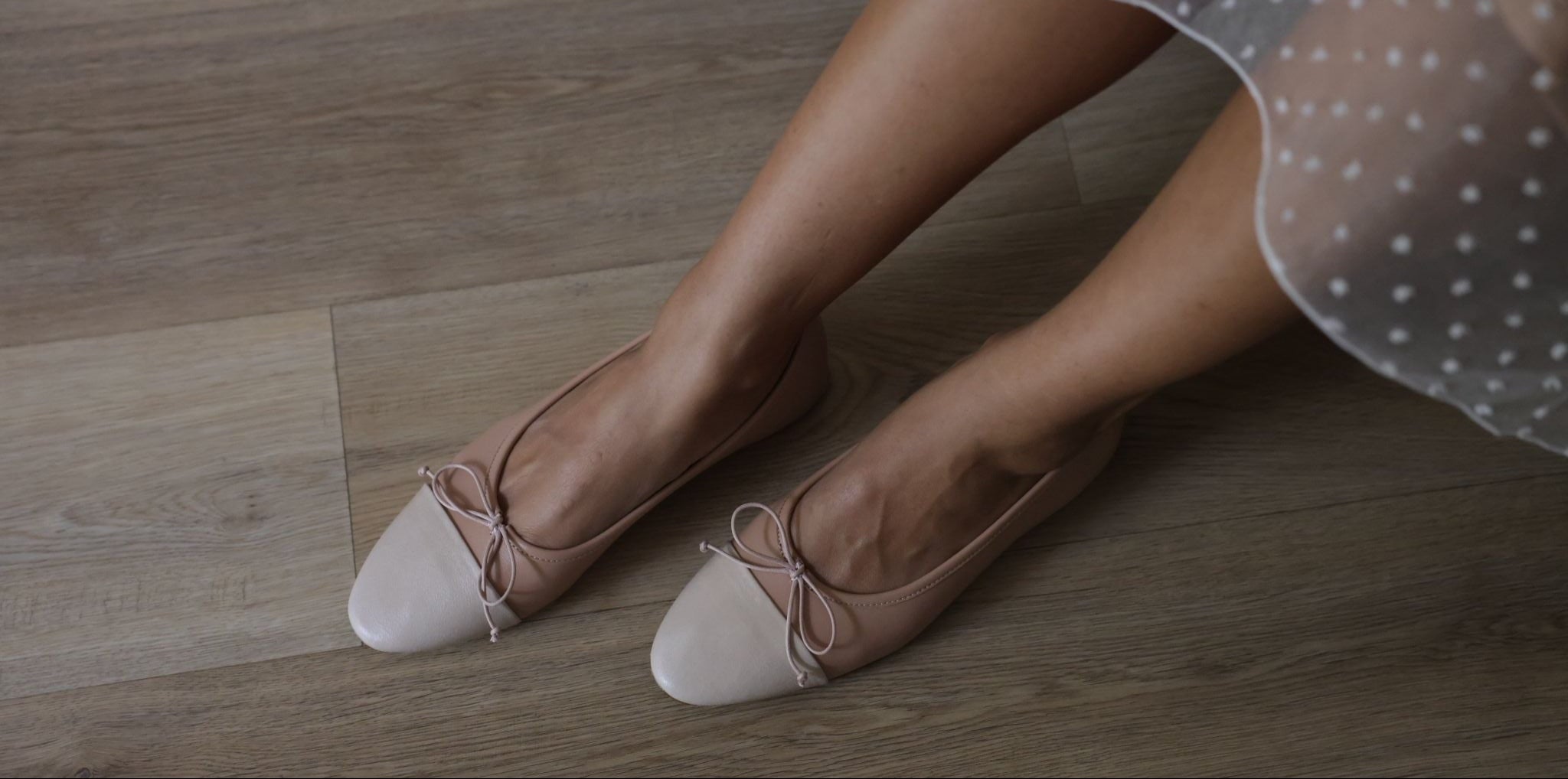 Person wearing a polka dot dress and beige shoes with bows on a wooden floor.